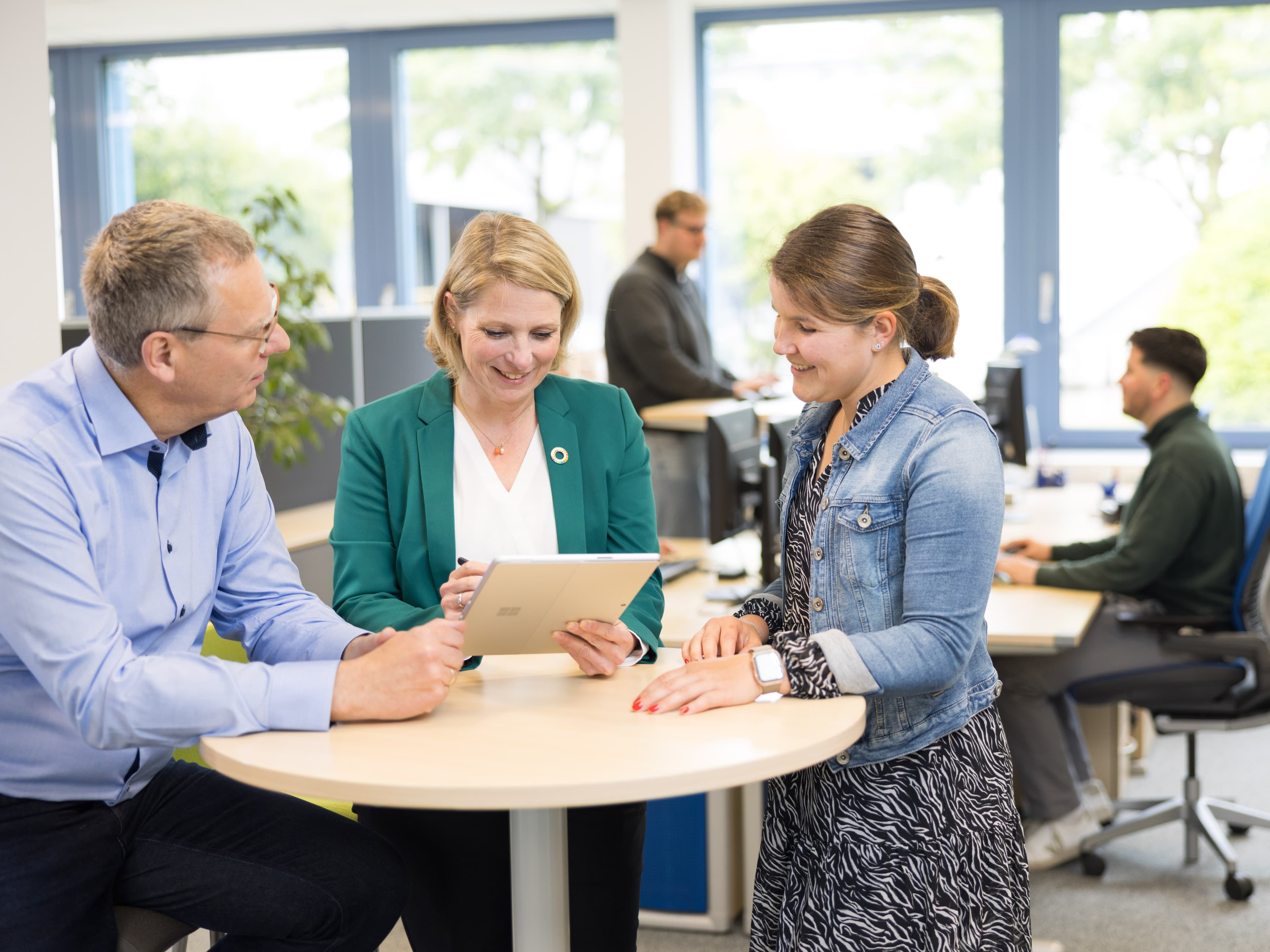 Specialists discuss project documents at a conference table in a modern office, with team members working in the background.