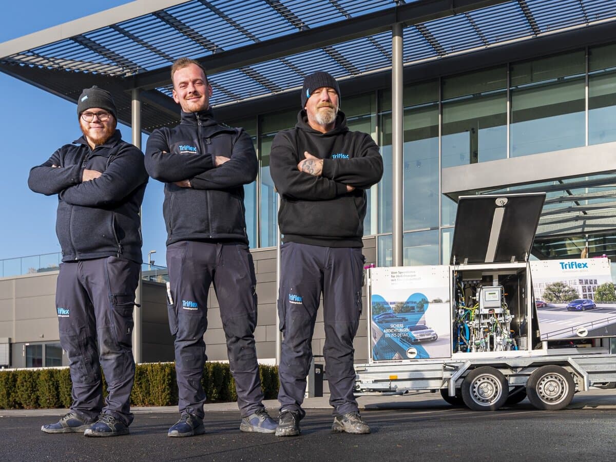 Three Triflex specialists standing next to a mobile SAM 2K spray application system.