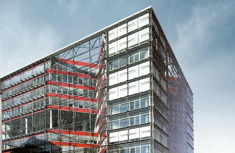 A modern building facade made of glass and steel with red structural elements in an urban setting