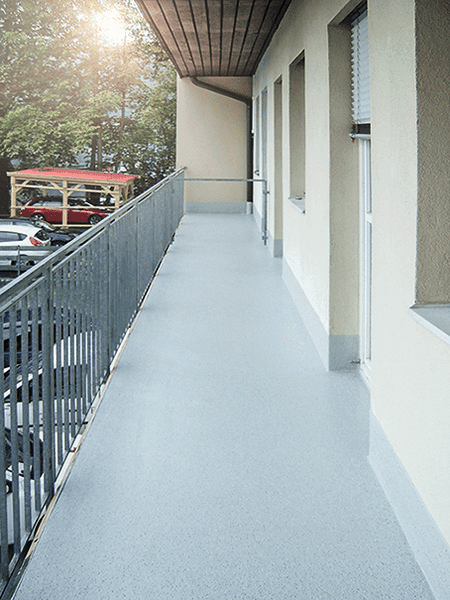 Sanierter Balkon‑Laubengang eines Wohngebäudes mit rutschhemmender, hellgrauer Beschichtung und Metallgeländer für langlebige Nutzung im Außenbereich.