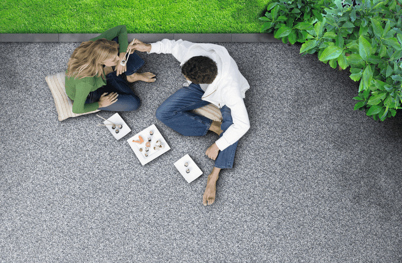 Pärchen sitzt auf einer Terrasse mit Triflex Stone Design Bodenbelag in Natursteinoptik und genießt gemeinsam Snacks
