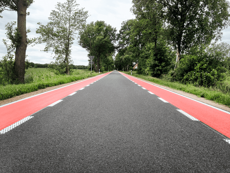 Sanierte Landstraße mit roter Randmarkierung für Radverkehr – langlebige Verkehrsflächenbeschichtung auf Asphalt zur sicheren Wegeführung im ländlichen Raum.