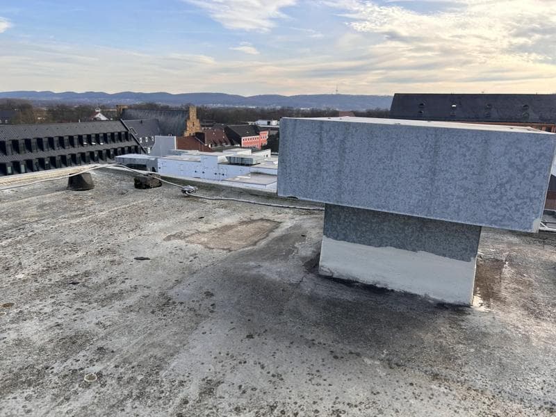 Abgedichteter Dachaufbau mit ummanteltem Aufsatz auf einer Flachdachfläche in Minden, mit Blick auf umliegende Gebäude und die hügelige Umgebung.
