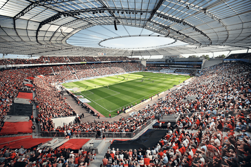 Großes Fußballstadion mit gefüllten Tribünen und überdachtem Spielfeld während einer Veranstaltung.