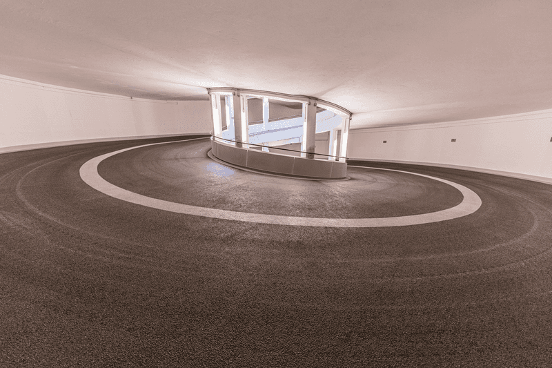 Rund verlaufende Parkhausrampe mit markierten Fahrspuren und beschichteter Oberfläche in einem hellen Innenbereich, fotografisch dargestellt.