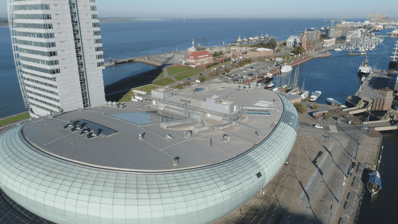 Drohnenaufnahme des Klimahaus Bremerhaven 8° Ost und der umliegenden Hafenpromenade mit Blick auf die Wesermündung und moderne Architektur im Überseehafen.